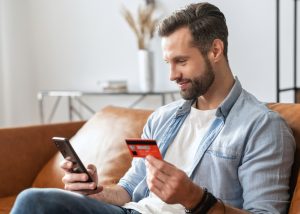 A man sitting on a brown sofa making a payment with his credit card