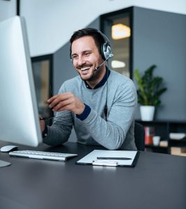 A customer service representative man wearing headphone at his desk attending the call with a smile on his face