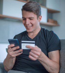 A smiling man making an online payment with his credit card from a mobile phone